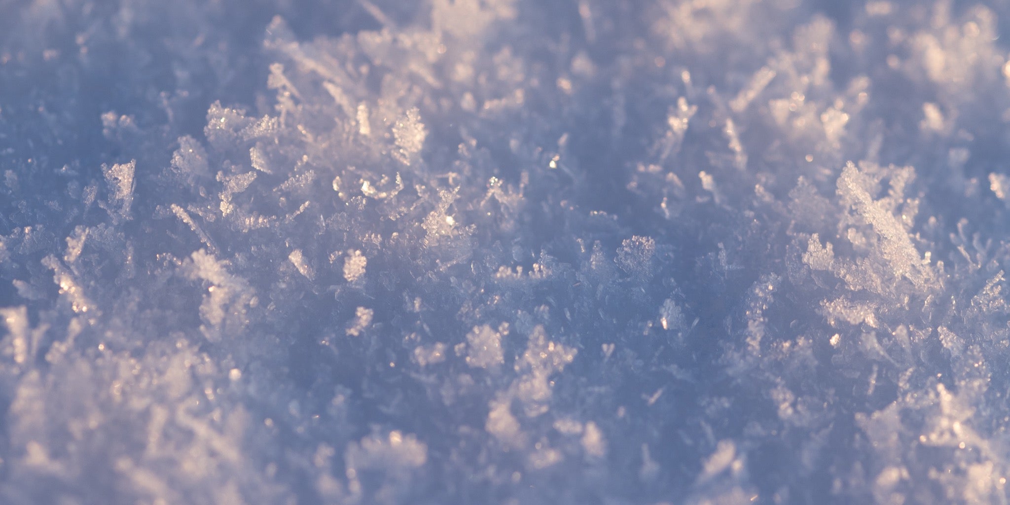 A close-up view of snow crystals, showcasing their intricate and delicate structures, illuminated by soft, pinkish light, creating a sparkling and frosty texture.